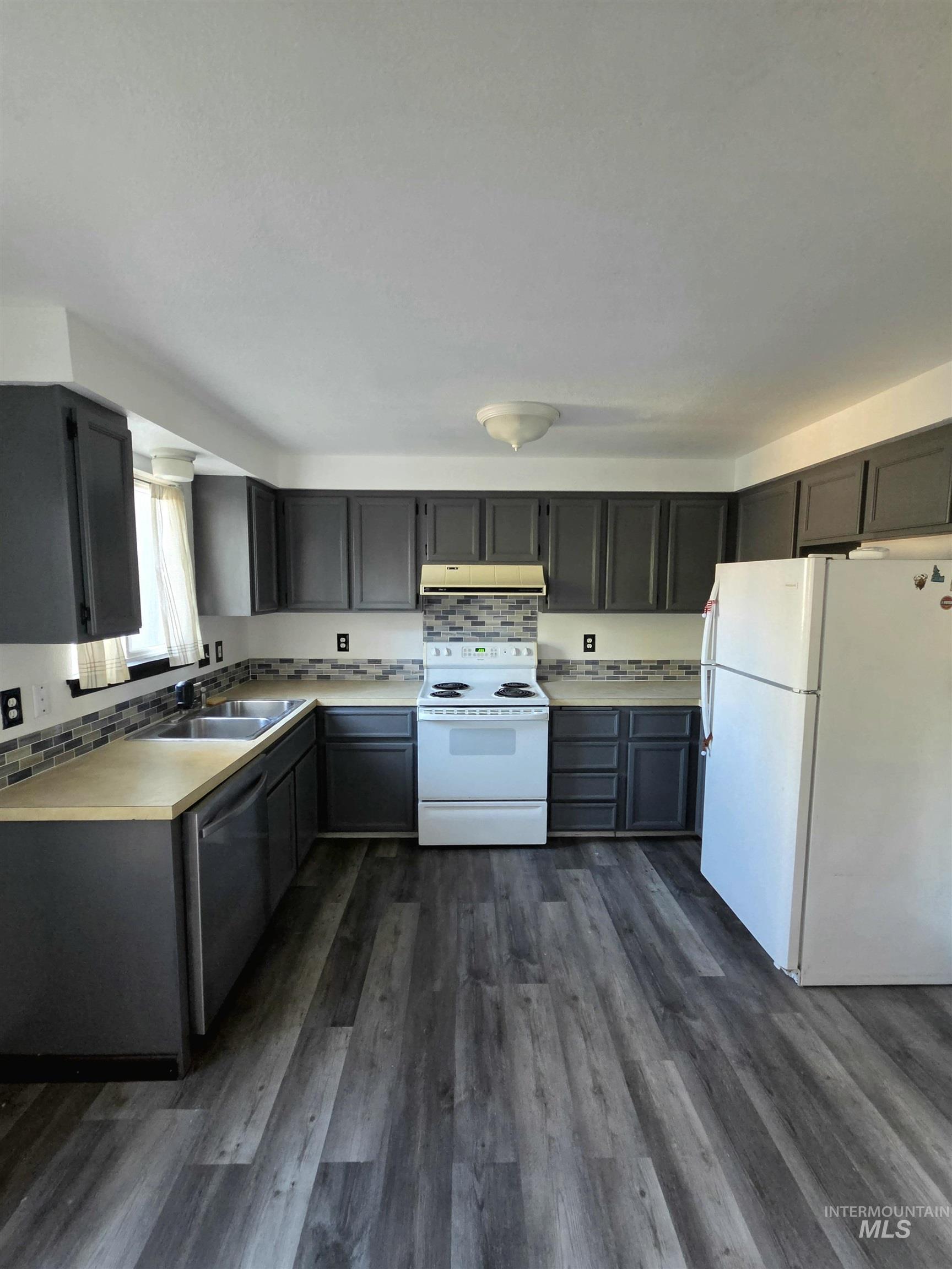 Spacious kitchen featuring wood-finish flooring, dark grey cabinetry, light countertops, and a tile backsplash
