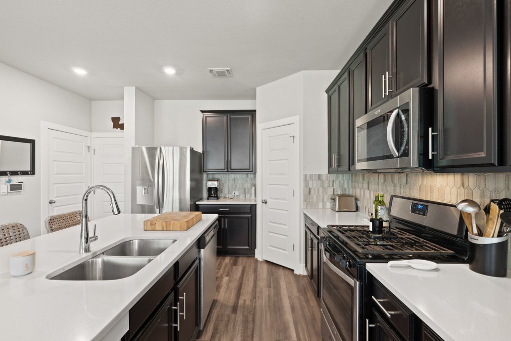7403 Travertine Spring Drive, Unit 117 Austin, TX 78744 - Photo 14 of 37 A contemporary kitchen features dark cabinetry, light countertops, and stainless steel appliances, creating a striking contrast.