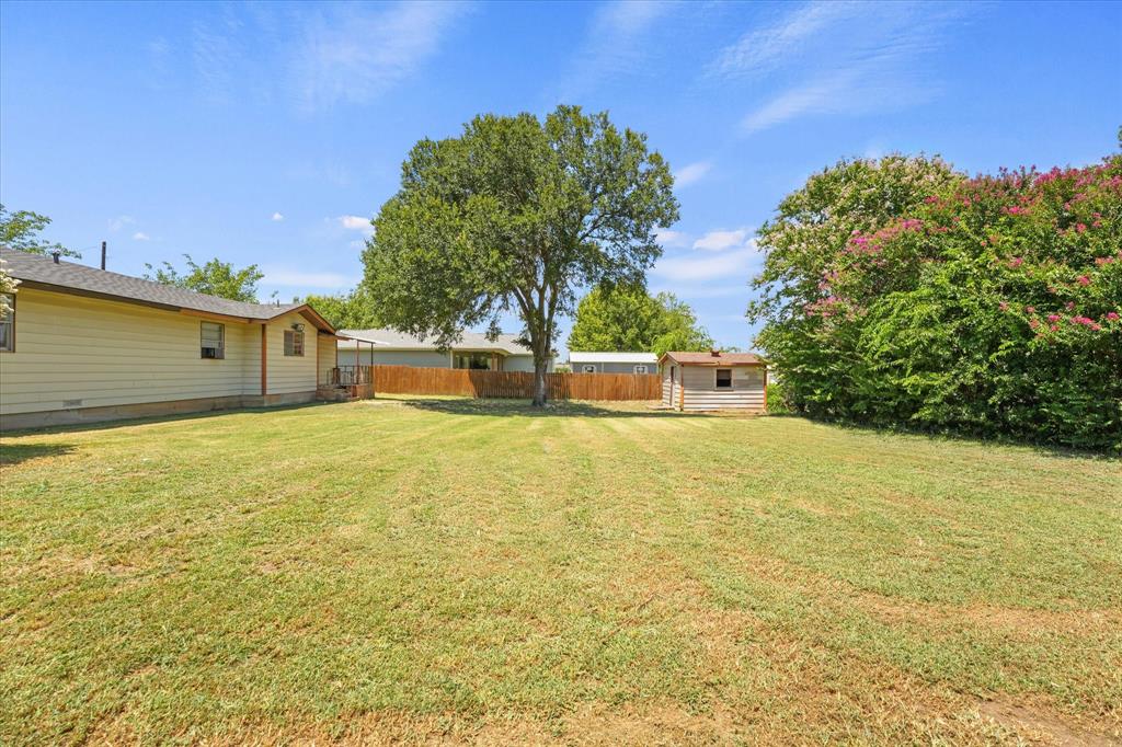 1100 North Church Street Decatur, TX 76234 - Photo 12 of 14 Expansive backyard featuring a large green lawn, mature trees, a privacy fence, and an outdoor storage shed