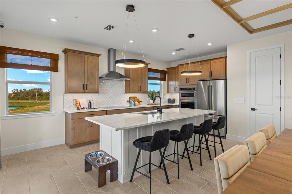 12785 Jade Empress Loop, Unit 202 Venice, FL 34293 - Photo 15 of 42 a kitchen with stainless steel appliances a sink a stove a refrigerator cabinets and a dining table with wooden floor