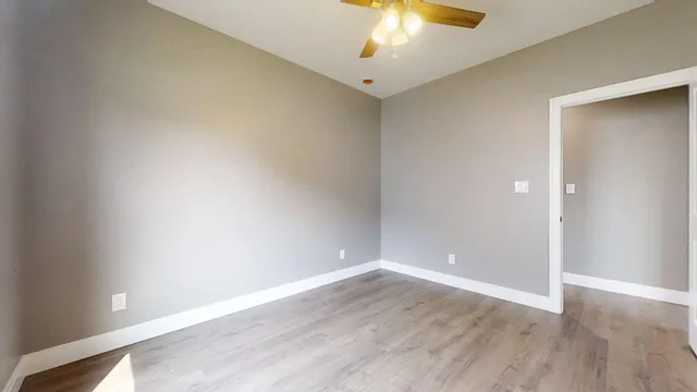 an empty room with wooden floor and a ceiling fan