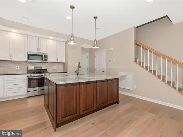 a kitchen with stainless steel appliances granite countertop a refrigerator a sink dishwasher a stove with white cabinets and wooden floor