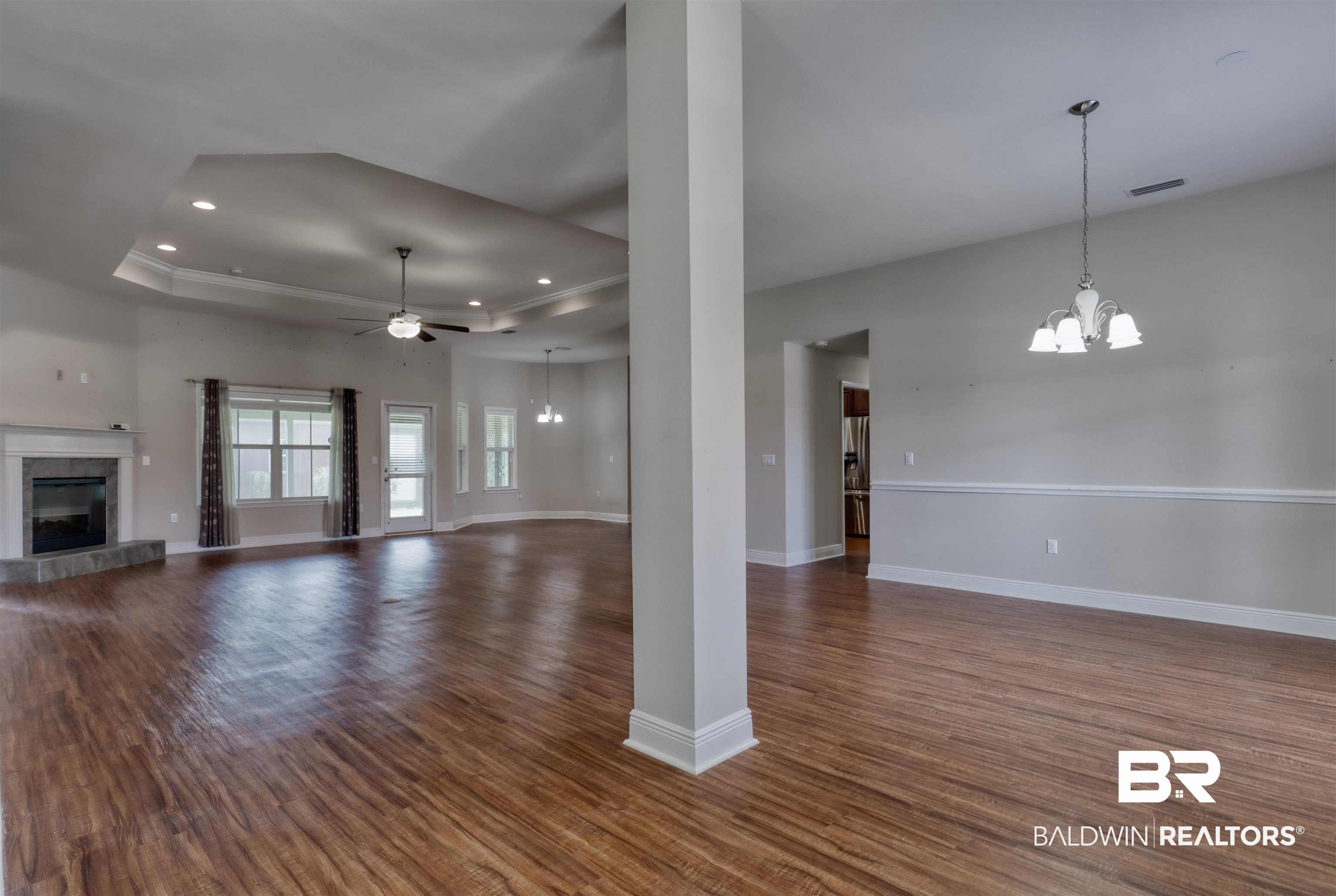 14794 Troon Drive Foley, AL 36535 - Photo 3 of 33 Unfurnished living room featuring dark wood-style flooring, a tray ceiling, baseboards, and ceiling fan with notable chandelier