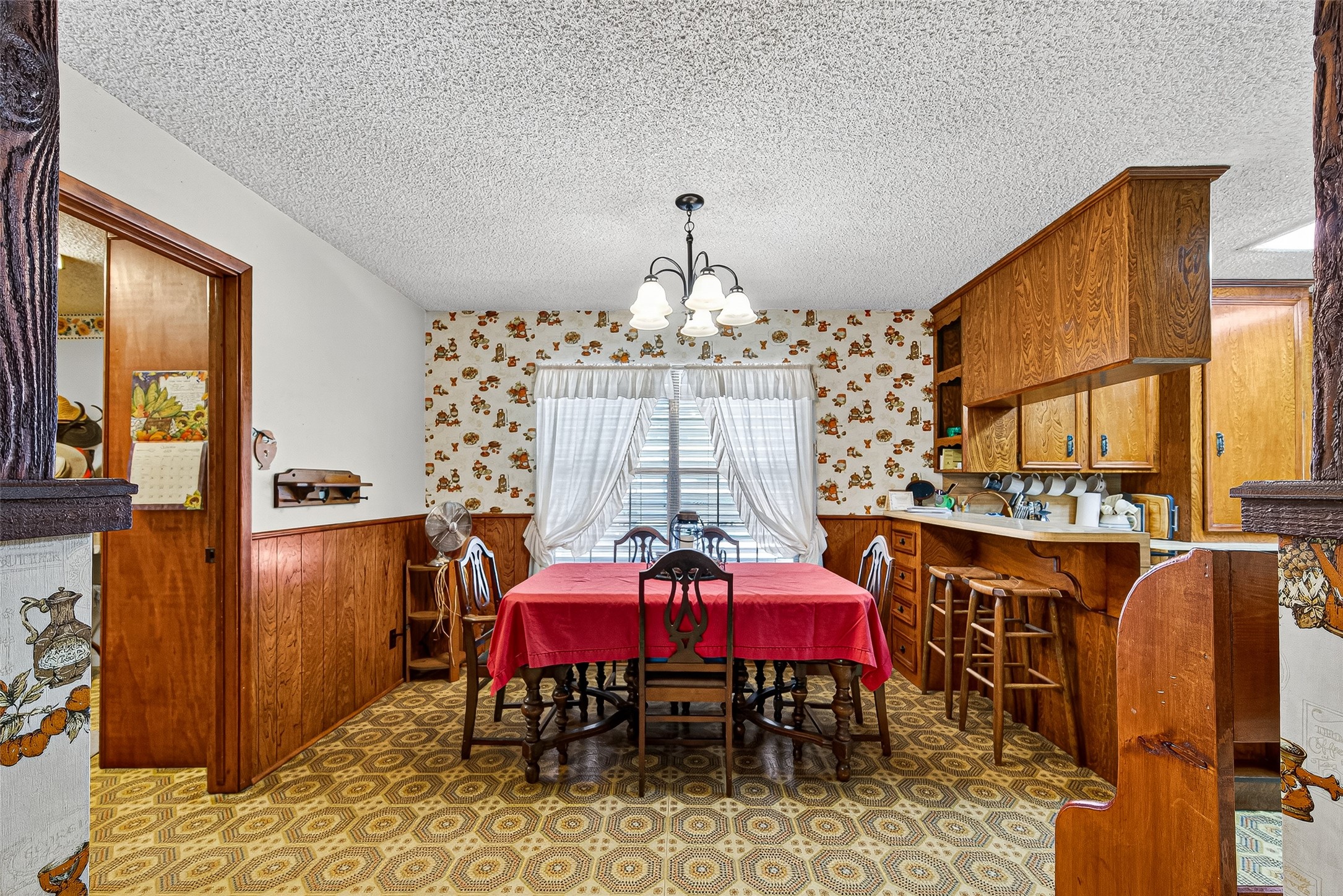 12021 7th 1/2 Street Santa Fe, TX 77510 - Photo 19 of 49 This cozy dining area features vintage charm with floral wallpaper and wood paneling A built-in kitchen nook with ample storage and counter space. A window with drapes allows natural light to brighten the space.