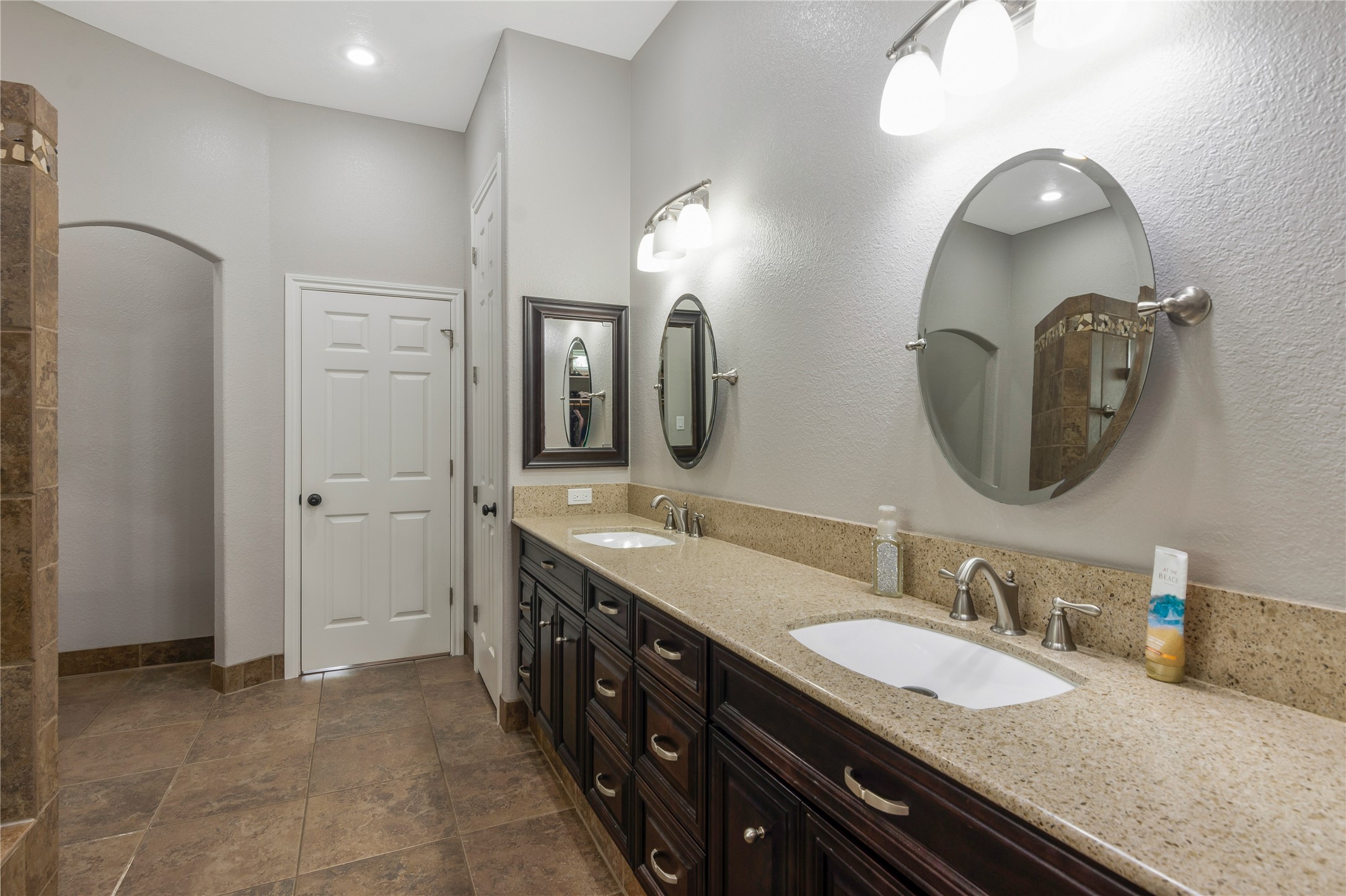 13914 Skinner Road Cypress, TX 77429 - Photo 18 of 50 Primary bathroom with a long granite vanity, dark wood cabinetry, round mirrors, and a walk in shower.