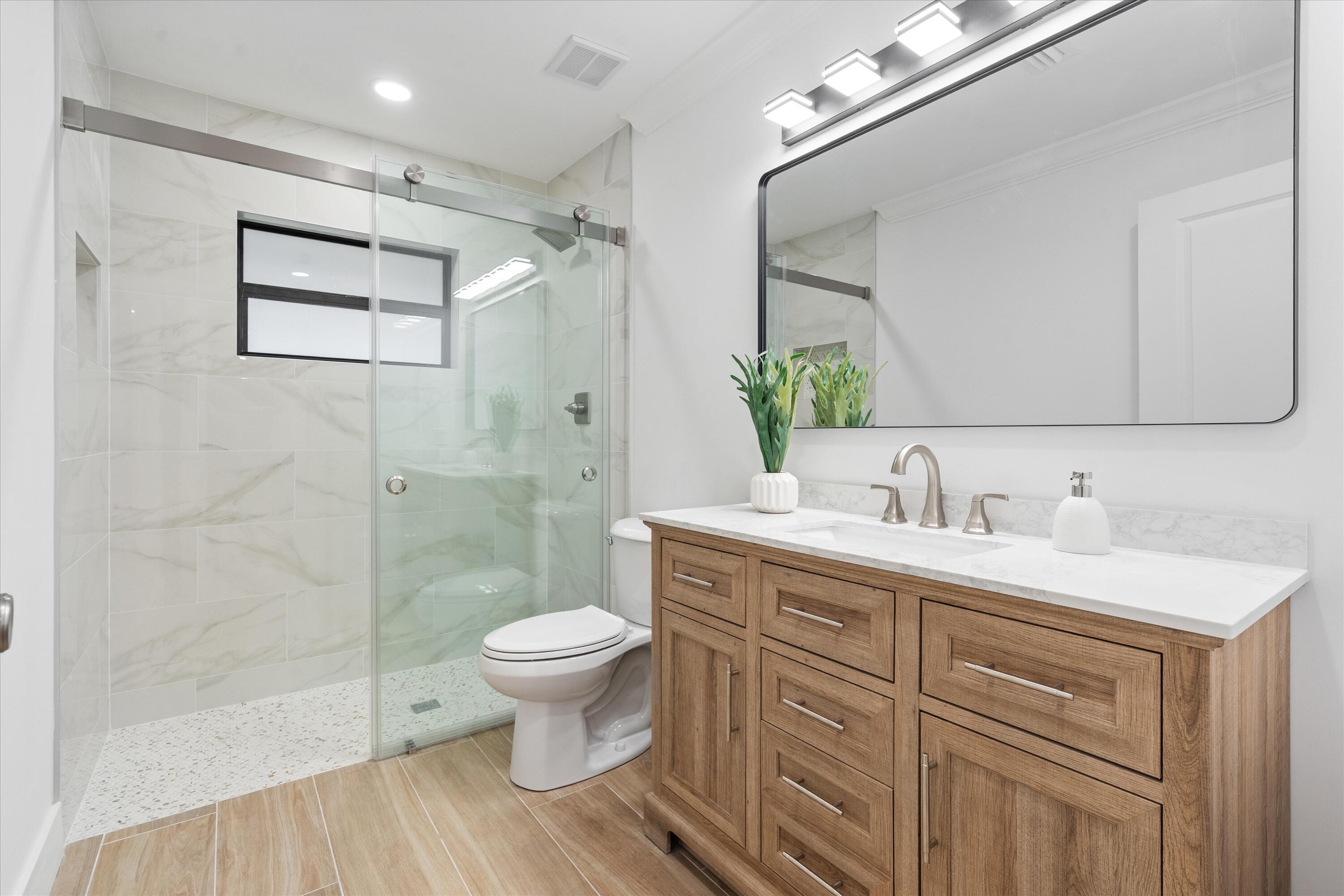 24 Dunbar Road Palm Beach Gardens, FL 33418 - Photo 57 of 93 a bathroom with a granite countertop sink toilet a mirror a vanity and shower