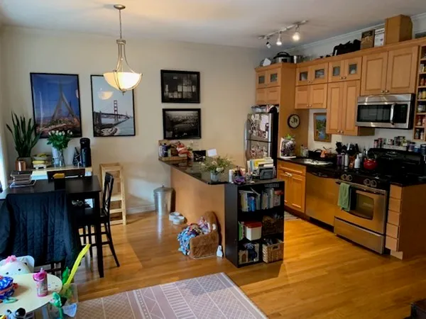 a kitchen with stainless steel appliances granite countertop a refrigerator a stove top oven a dining table and chairs with wooden floor