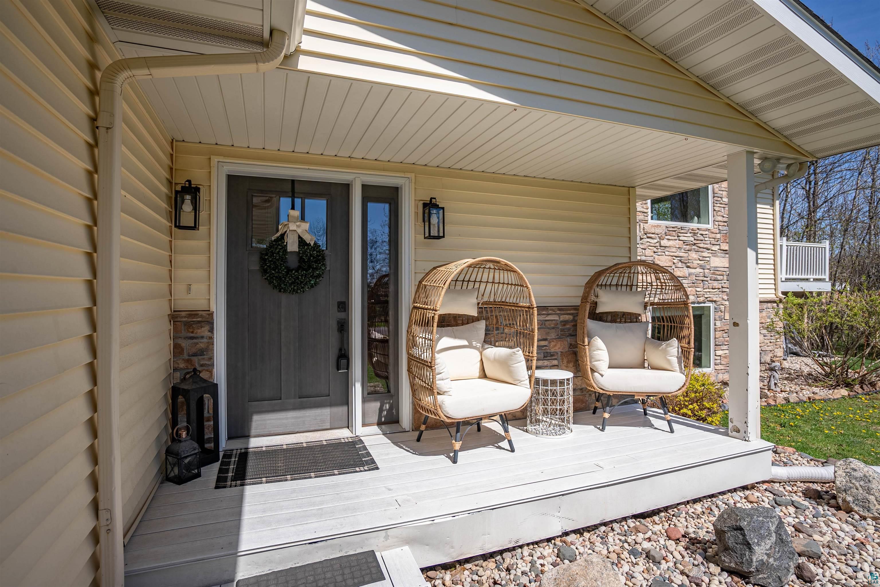 4809 Oak Ridge Drive Hermantown, MN 55811 - Photo 3 of 69 Covered front porch featuring a dark gray entry door with decorative glass, two wall-mounted lanterns, light-colored siding, stone accents, and a white porch floor