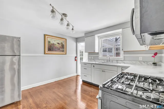 a kitchen with stainless steel appliances granite countertop a stove a sink dishwasher and white cabinets with wooden floor