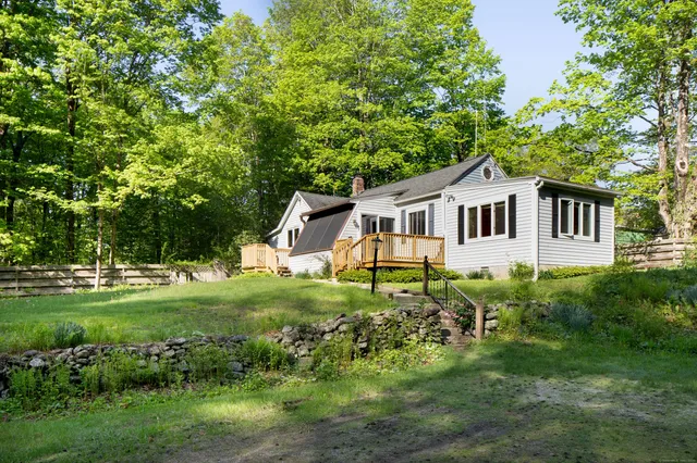 a white house with a big yard plants and large trees