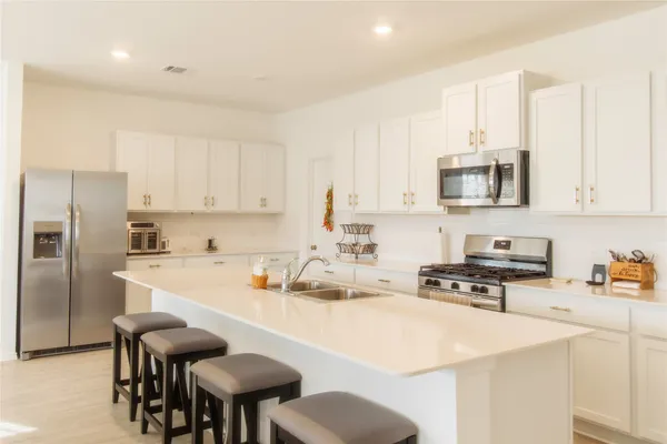 a kitchen with stainless steel appliances a stove a sink a microwave a refrigerator and white cabinets