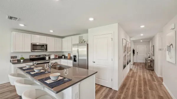 a kitchen with stainless steel appliances granite countertop a refrigerator a stove a sink a dining table and chairs with wooden floor