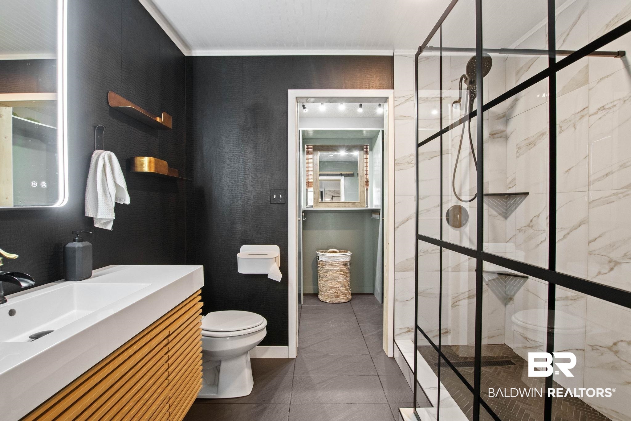 524 Ariel Avenue Foley, AL 36535 - Photo 17 of 37 Bathroom featuring a wood-finish vanity with an integrated sink, a frameless LED-backlit mirror, and a black-framed glass shower enclosure with marbled tile surround
