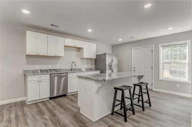 a kitchen with stainless steel appliances granite countertop a stove top oven a sink dishwasher and a refrigerator with wooden floor