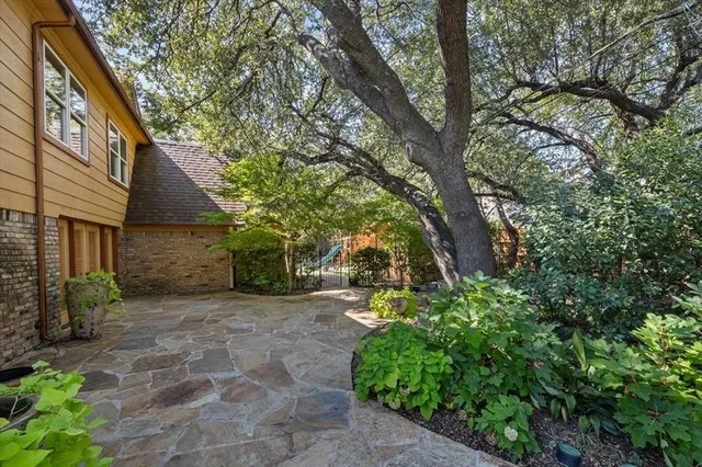 a pathway of a house with potted plants and large trees