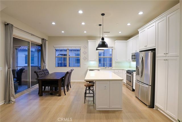 a kitchen with stainless steel appliances kitchen island granite countertop a refrigerator a sink dishwasher a dining table and chairs with wooden floor
