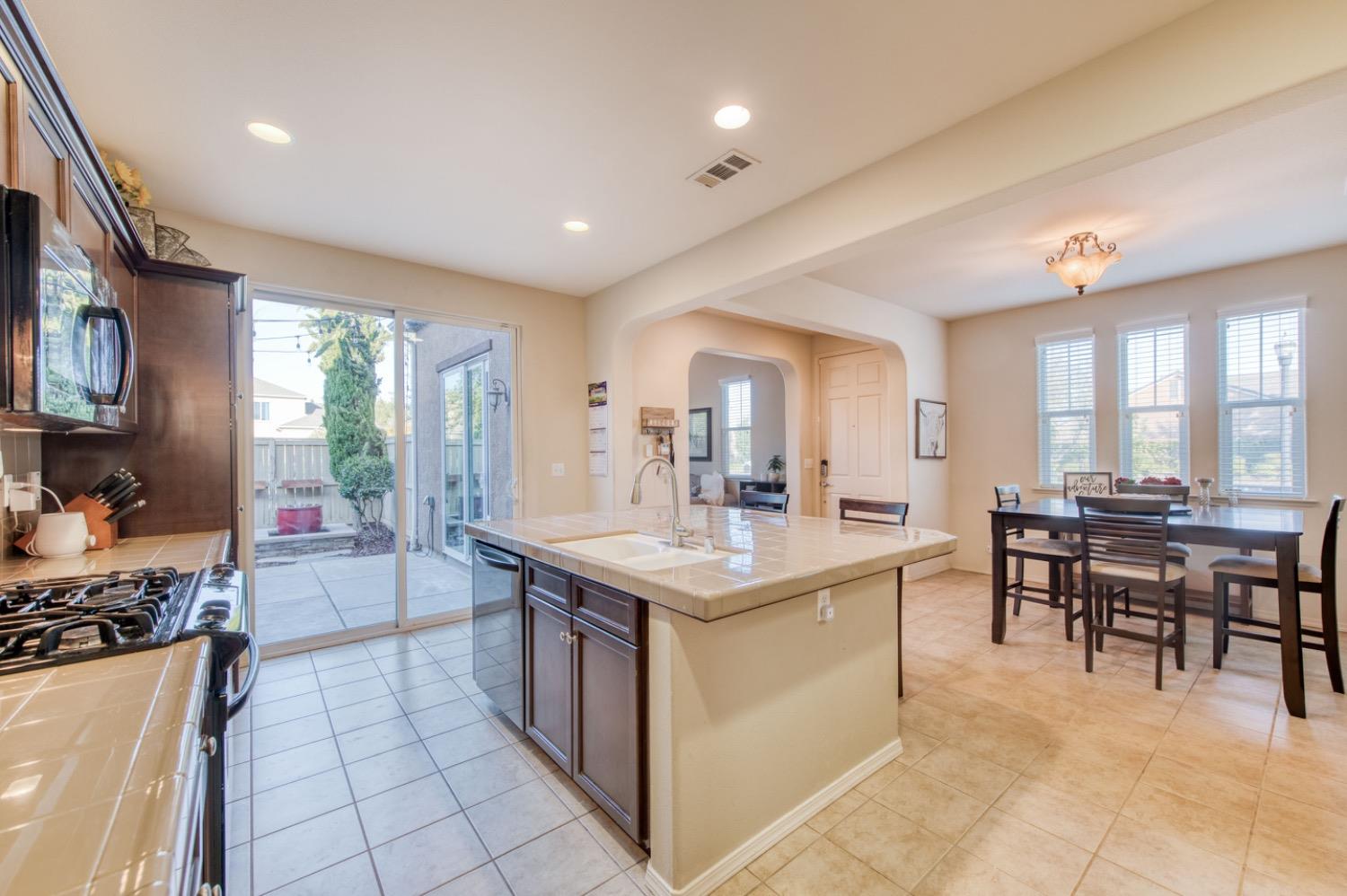 4085 Harlan Ranch Boulevard Clovis, CA 93619 - Photo 8 of 27 a large kitchen with kitchen island a sink and a stove a dining table and chairs with wooden floor