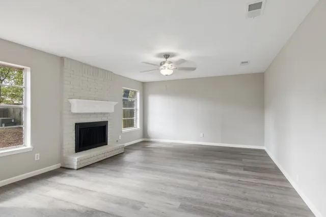 a view of an empty room with wooden floor fireplace and a window
