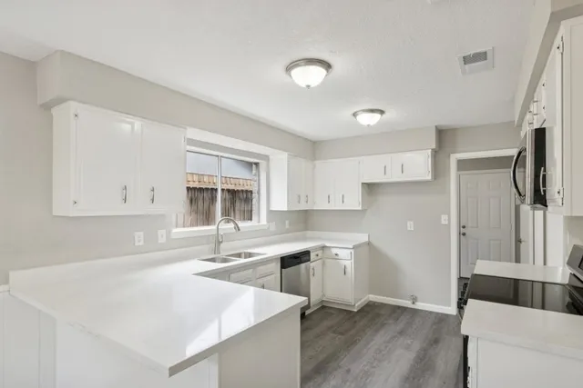 a kitchen with a sink dishwasher a stove and white cabinets with wooden floor