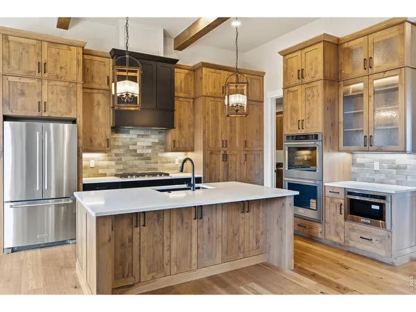 a kitchen with stainless steel appliances granite countertop a refrigerator a stove and a sink with wooden floors
