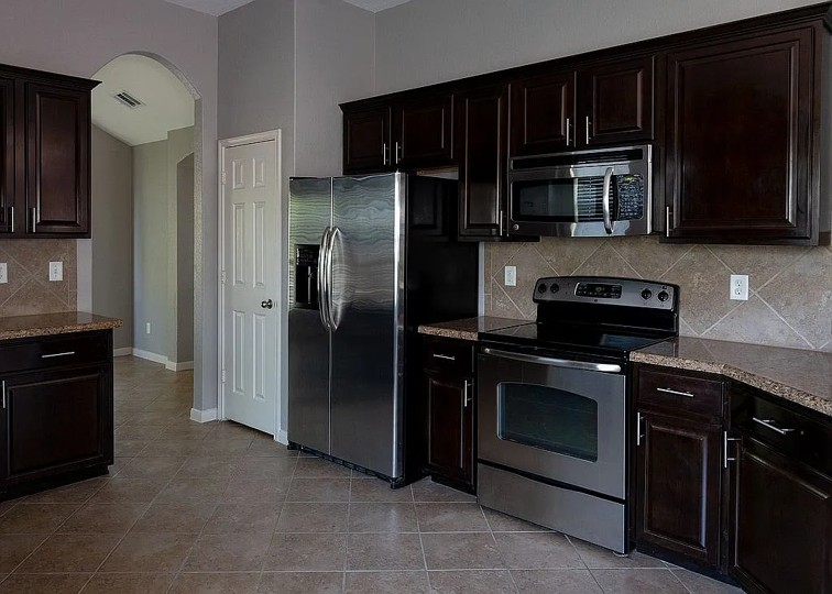 7703 Redstone Manor Converse, TX 78109 - Photo 6 of 28 Kitchen featuring decorative backsplash, dark wood finish cabinets, stainless steel appliances, arched walkways, and light tile patterned flooring