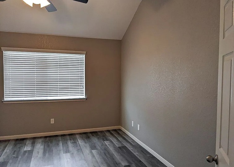 7703 Redstone Manor Converse, TX 78109 - Photo 9 of 28 Empty room featuring ceiling fan, wood finished floors, a textured wall, and vaulted ceiling