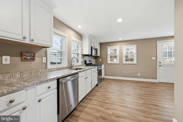 a large kitchen with granite countertop a stove a sink a refrigerator and white cabinets with wooden floor