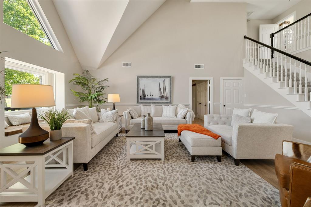 12240 Wellington Road Ponder, TX 76259 - Photo 7 of 40 Spacious living area featuring vaulted ceilings, abundant natural light from large windows and an additional transom window, a built-in window bench, a grand staircase with white spindles and a dark handrail, and light wood-finish flooring