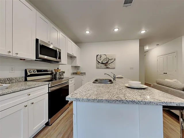 a kitchen with granite countertop stainless steel appliances a sink a stove top oven a counter space and cabinets