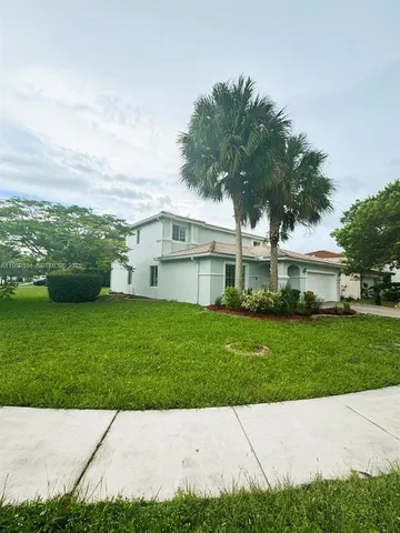 a view of a white house next to a yard with big trees