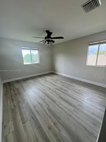 an empty room with wooden floor fan and windows
