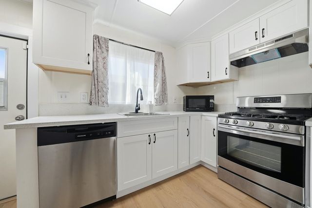a kitchen with stainless steel appliances white cabinets granite counter tops and a window