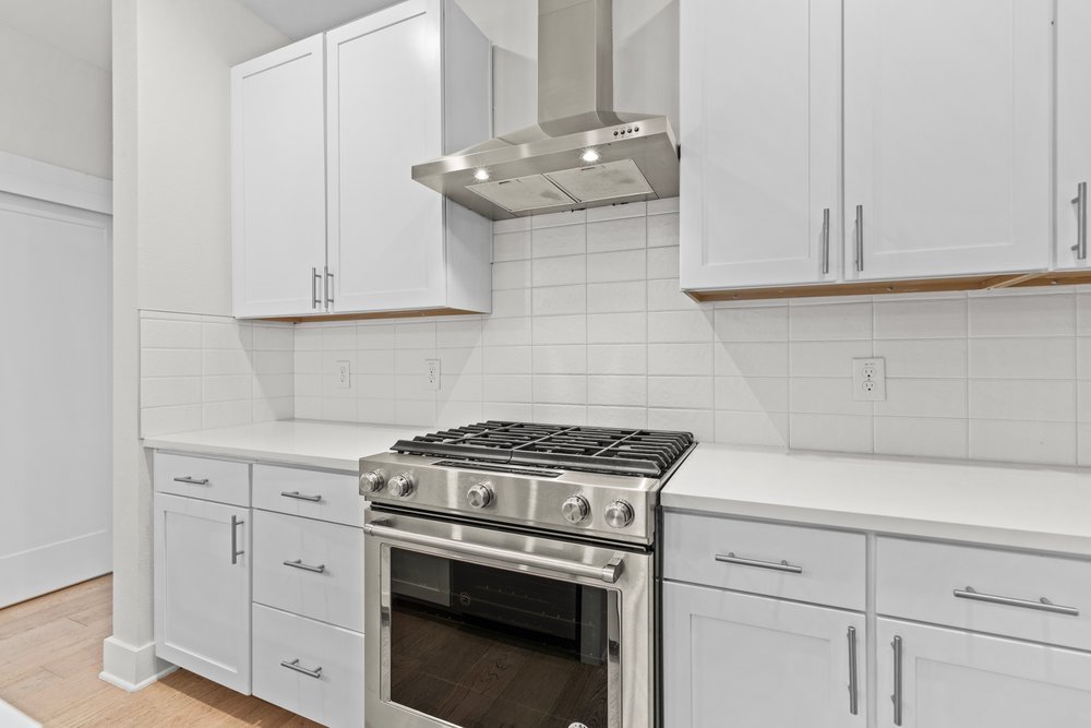 2827 Manor Road, Unit 2201 Austin, TX 78722 - Photo 16 of 40 Modern kitchen featuring stainless steel gas range, coordinating range hood, white shaker-style cabinetry, light-toned countertops, and white subway tile backsplash