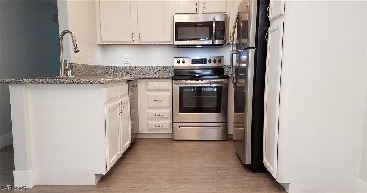 Kitchen featuring appliances with stainless steel finishes, dark stone countertops, white cabinetry, and light wood-style flooring