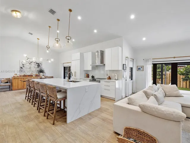 a large white kitchen with a large counter top a sink stainless steel appliances and cabinets