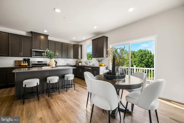 a open dining room with stainless steel appliances a dining table wooden floor and a kitchen view