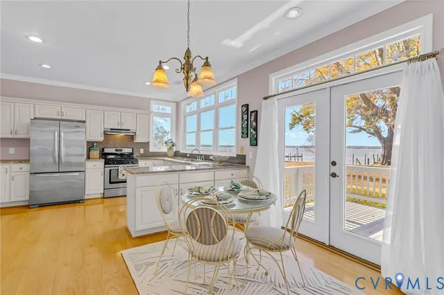 a kitchen with stainless steel appliances granite countertop a stove a refrigerator a sink a dining table and chairs with wooden floor