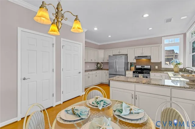 a kitchen with stainless steel appliances granite countertop a sink a stove a dining table and chairs with wooden floor