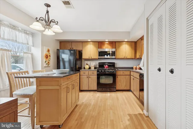 a kitchen with stainless steel appliances granite countertop a stove top oven a sink dishwasher and a refrigerator with wooden floor