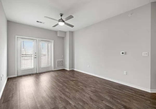 a view of an empty room with wooden floor and a ceiling fan