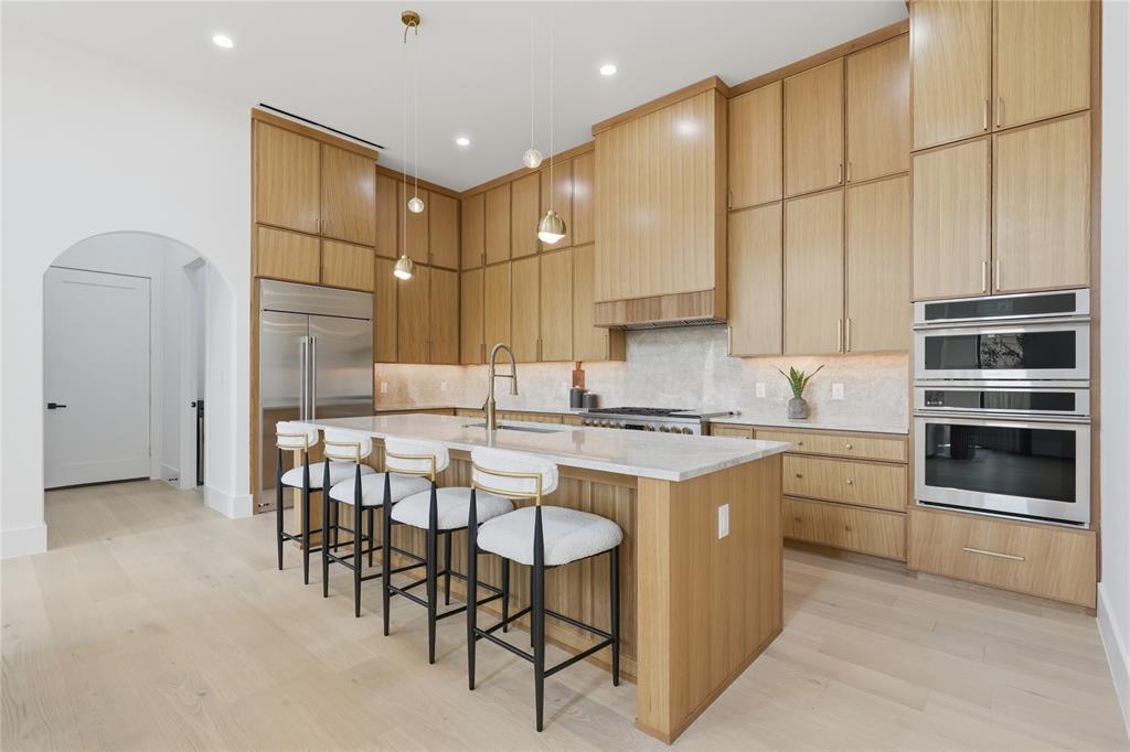 6038 Prospect Avenue Dallas, TX 75206 - Photo 10 of 40 Contemporary kitchen featuring light wood-finish cabinetry, a large center island with seating, integrated stainless steel appliances, and sleek pendant lighting
