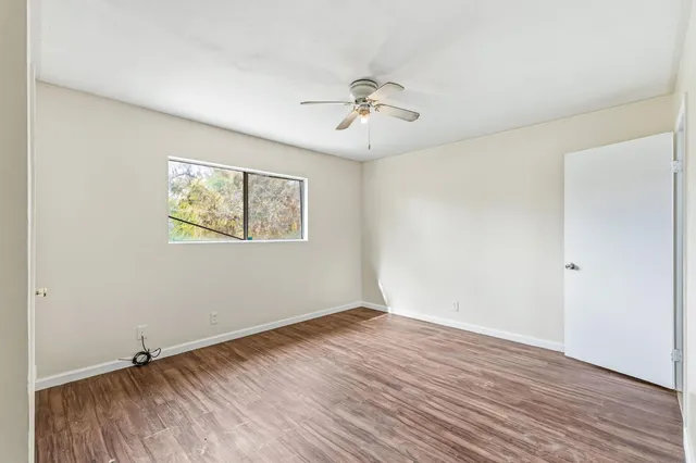 an empty room with wooden floor ceiling fan and windows