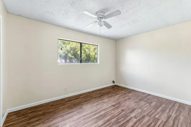 an empty room with wooden floor ceiling fan and windows