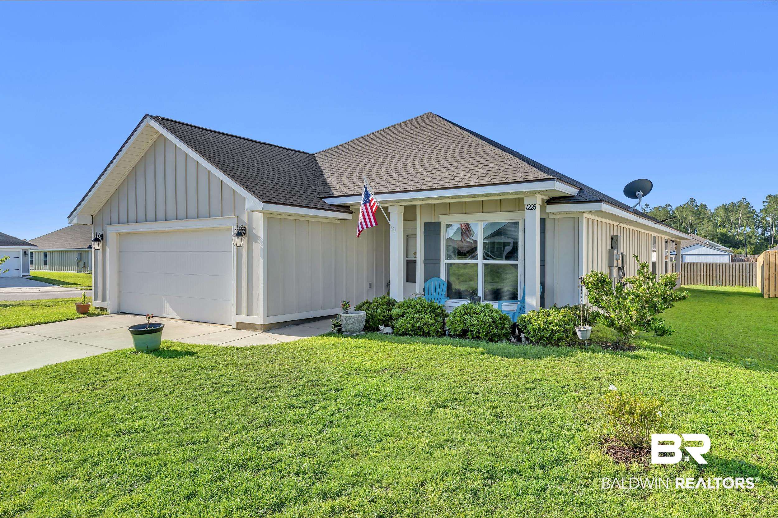 1228 Caper Avenue Foley, AL 36535 - Photo 3 of 54 Single-story residence featuring light-colored vertical siding, a dark shingle roof, an attached two-car garage with a panel door, a concrete driveway, and a front porch with a prominent window