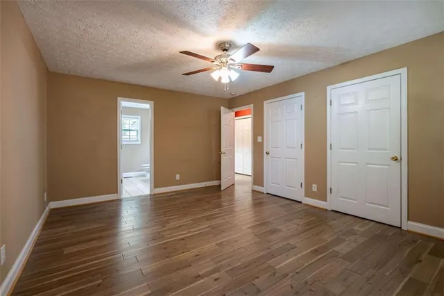 a view of an empty room with wooden floor and a ceiling fan