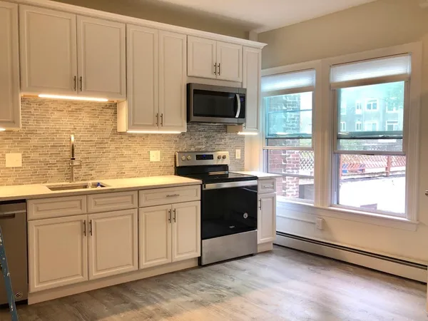 a kitchen with stainless steel appliances granite countertop white cabinets a sink a stove a microwave and a window