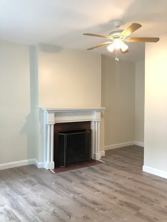 a view of an empty room with wooden floor fireplace and a window