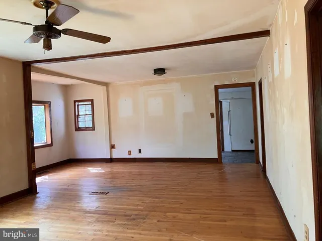 a view of an empty room with wooden floor and a ceiling fan