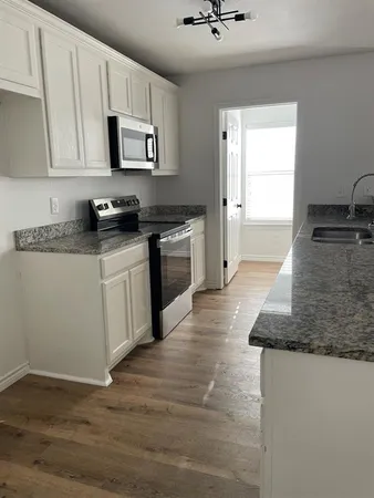 a kitchen with granite countertop a stove top oven a sink dishwasher and white cabinets with wooden floor