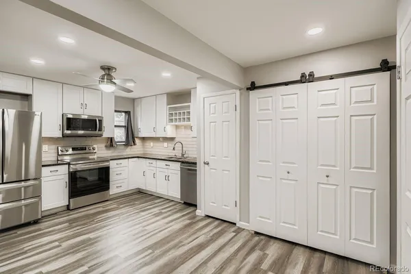 a kitchen with granite countertop a refrigerator oven a sink dishwasher and white cabinets with wooden floor